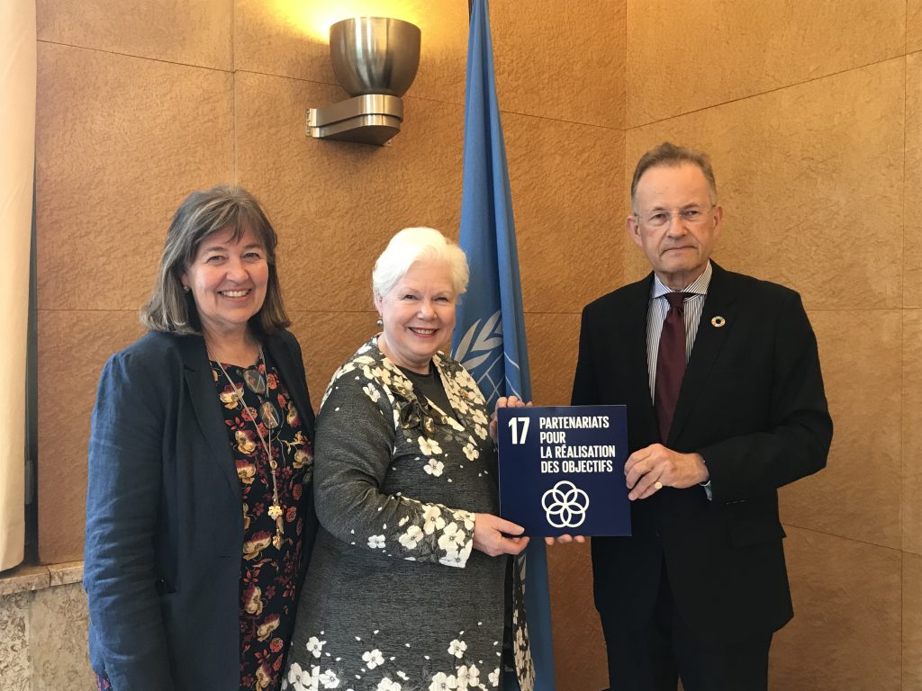 The Lieutenant Governor stands with two United Nations employees holding a dark blue SDG card titled SDG 17 Partnerships for the Goals