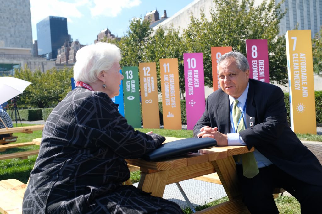 The Lieutenant Governor and Dr. Peter Singer sit at a picnic table with the SDGs in the background